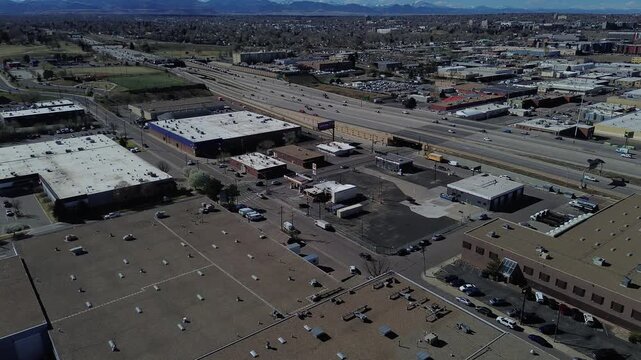 Highway corridor span highlights commercial blocks near W 4th Ave multilane traffic moving toward Denver skyline snowtipped Front Range. Mixed roofing, muted tones, manufacturing, fleet services