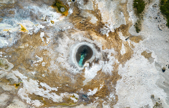 Aerial view of Hveravellir geothermal area featuring a steaming hot spring with turquoise water surrounded by mineral crusts and volcanic terrain in Hunabyggd, Iceland.