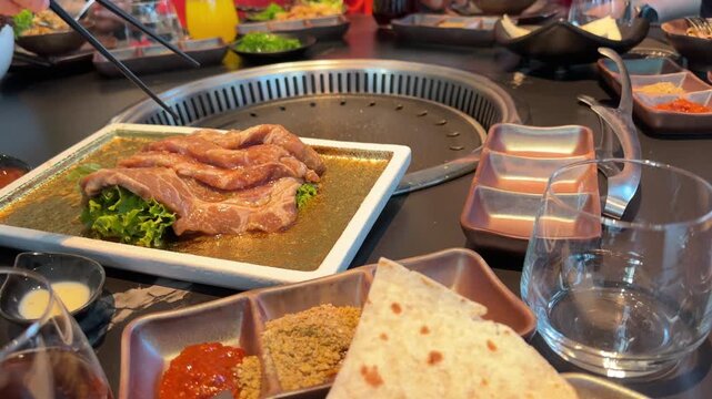 Raw meat slices and chicken, beef and squid pieces cooking tabletop built in asian barbecue grill restaurant, grilling on hot metal plate, BBQ cooking process, Group friends enjoying delicious food
