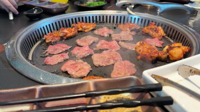 Raw meat slices and chicken, beef and squid pieces cooking tabletop built in asian barbecue grill restaurant, grilling on hot metal plate, BBQ cooking process, Group friends enjoying delicious food
