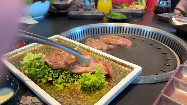 Raw meat slices and chicken, beef and squid pieces cooking tabletop built in asian barbecue grill restaurant, grilling on hot metal plate, BBQ cooking process, Group friends enjoying delicious food