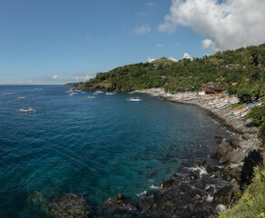 Fototapeta premium View of a tropical bay in Bunutan, east Bali, Indonesia, with clear blue water, a rocky shore and rows of traditional fishing boats along the coast.