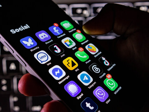 Closeup of a smartphone screen displaying various social media and communication app icons held in a persons hand
