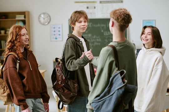 Teenagers greeting and chatting in classroom, building peer connection and school friendship before lesson