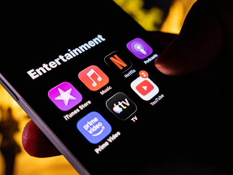 Closeup of a smartphone screen showing various entertainment apps like netflix, youtube, apple music, and prime video, held by a person
