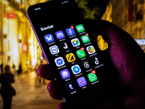 Closeup of a person holding a smartphone displaying various social media and communication app icons on the screen at night