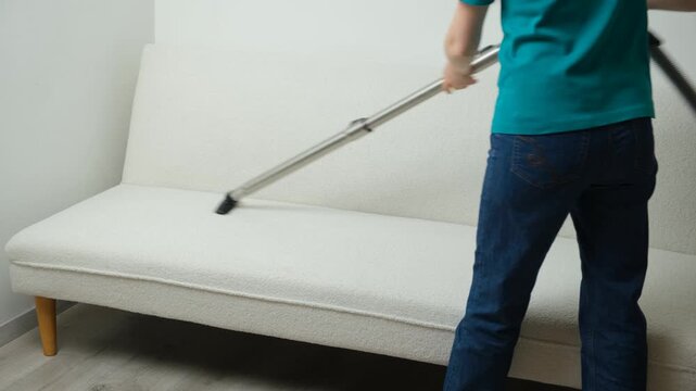 Woman cleaning white sofa with vacuum cleaner nozzle close up.
