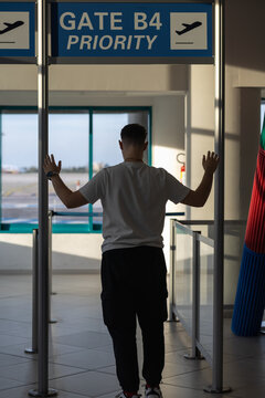 back view of a young traveler man standing at airport gate b4 priority entrance, looking at the runway through the window, ready for summer vacation