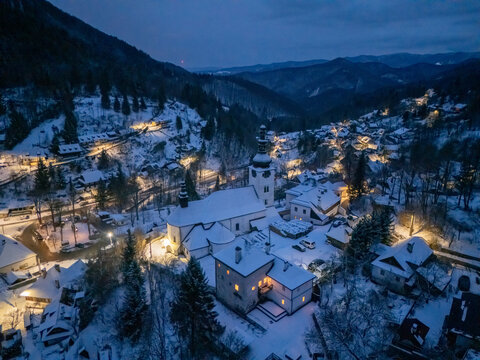 Aerial view of the historic church and illuminated houses nestled in a snow-covered mountain valley at night Spania Dolina, Banska Bystrica Region, Slovakia.