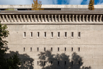 Obraz premium A flat, front-on architectural shot of a massive brutalist concrete wall featuring a rhythmic, repeating pattern of small vertical windows and structural facade details under a blue sky.