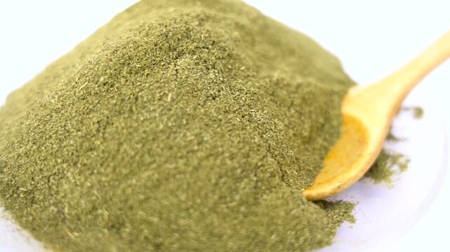 Close-up of a large mound of finely ground green powder with a small wooden spoon resting inside, presented on a bright white background herb spice food ingredient organic, moringa powder