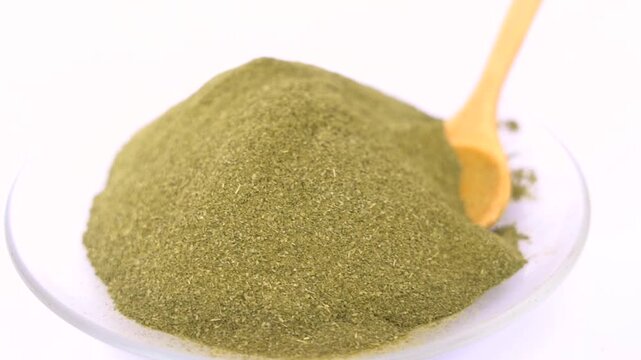 Close-up shot of a large pile of finely ground green powder served on a transparent glass plate with a small wooden spoon, highlighting natural ingredients herb spice food ingredient organic,  moringa