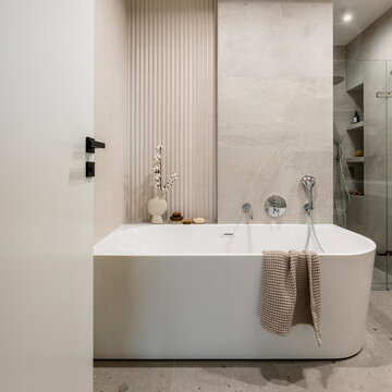 Modern bathroom interior with white freestanding bathtub, elegant fixtures, textured walls, and natural light for relaxation