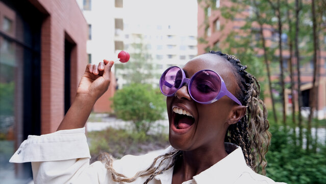 A beautiful woman poses for a smartphone selfie, holding a sweet lollipop.