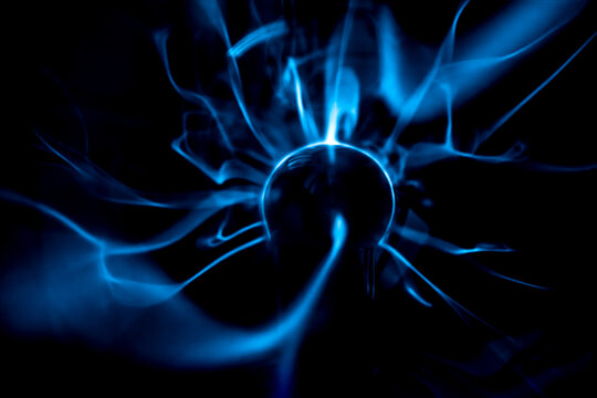 Close-up of a plasma ball globe glowing with blue and purple light and energy electricity rays on a black background