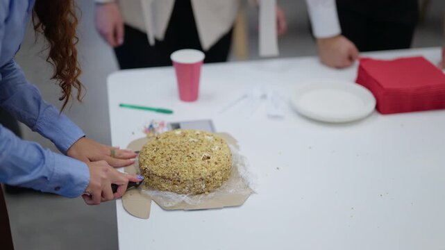 A woman slices a cake for her coworkers at an office celebration. Businesspeople gather around a table with a festive cake.