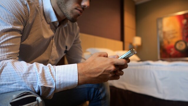 Male entrepreneur browsing modern smartphone while sitting in modern hotel room or apartment interior. Successful businessman using mobile technology showing communication and work routine. Slow mo