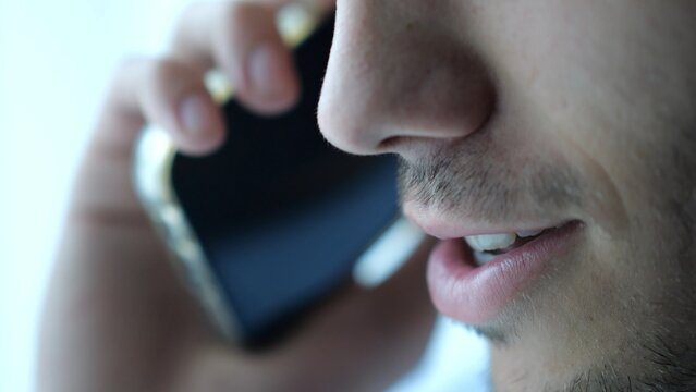 Close up male mouth speaking by smartphone near window with day light. Handsome bearded guy talking on phone at apartment. Young man having conversation on cellphone at office. Slow motion