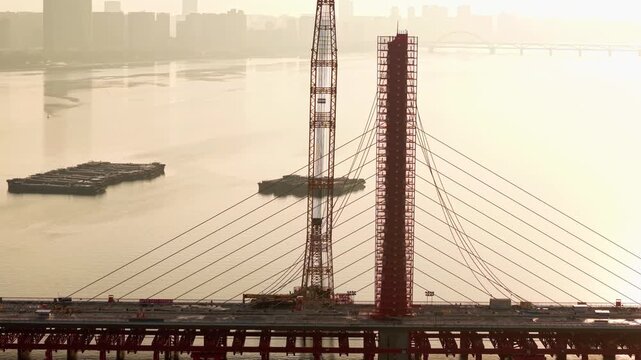 Aerial view of bridge demolition in China, cable-stayed structure being dismantled with cranes over river on the sunset