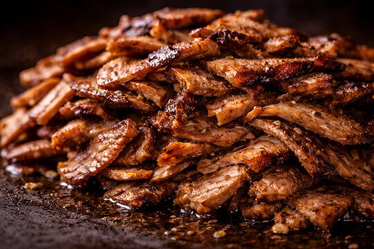 A high-angle close-up shot of a large pile of freshly grilled, thinly sliced, and seasoned beef shawarma meat, glistening with juices on a dark surface.