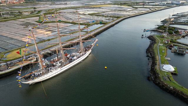 Aerial view of the tall ship NRP Sagres decorated with signal flags navigating the Canal de Aveiro near the salt pans Aveiro, Aveiro, Portugal.