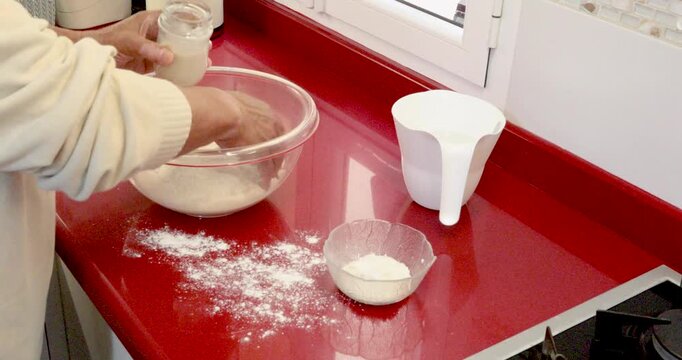 Adding Dissolved Yeast to Flour in Bowl for Homemade Focaccia Dough Preparation. Male hands pouring dissolved yeast into flour inside bowl during homemade focaccia dough preparation. 