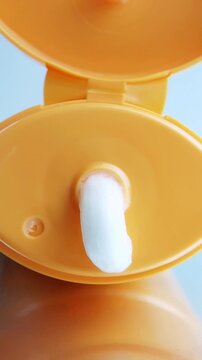 White cream that comes out slowly from the orange tube packaging above the glass reflection. Close up vertical captures are suitable for content beauty concepts