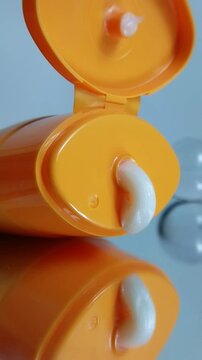 White cream coming out of orange packaging product on glass reflection. Vitamin C cream for the theme of maintaining healthy and natural skin