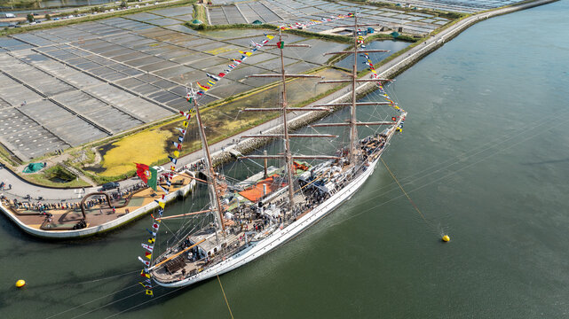 Aerial view of the tall ship NRP Sagres decorated with signal flags navigating the Canal de Aveiro near the salt pans Aveiro, Aveiro, Portugal.