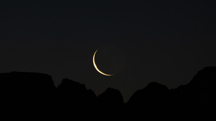 A sliver of the waning crescent moon rises above the rugged peaks of Zion NP Utah USA when the sky is just beginning to lighten on the morning of April 15th 2026. © Melani