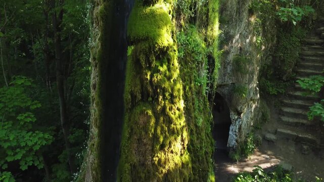 Artificial waterfall on stream flowing along rock overgrown with moss