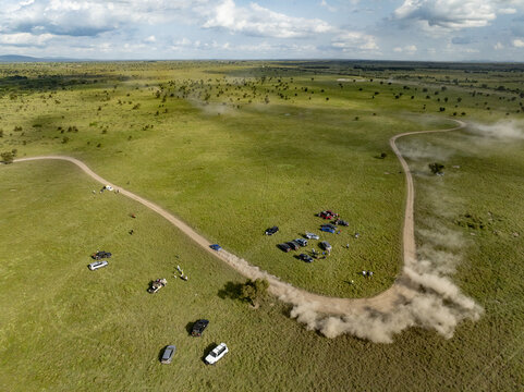 Aerial view of Swara Plains Conservancy with people standing near off-road vehicles on dirt tracks across the green savanna in Nairobi, Machakos County, Kenya.