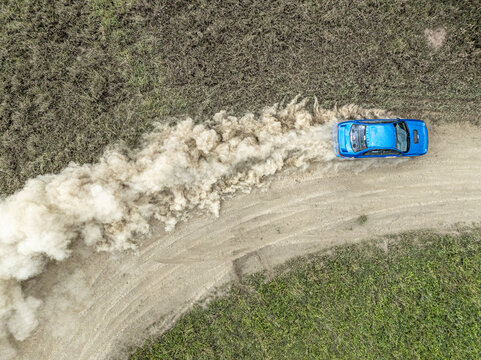 Aerial view of a blue rally car speeding on a dirt track and kicking up a massive cloud of dust in the Swara Plains Conservancy Nairobi, Machakos County, Kenya.