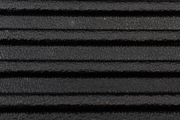Close-up texture of a black ribbed rubber mat or tough plastic truck bed liner with a rough, non-slip surface. © Thanaphon
