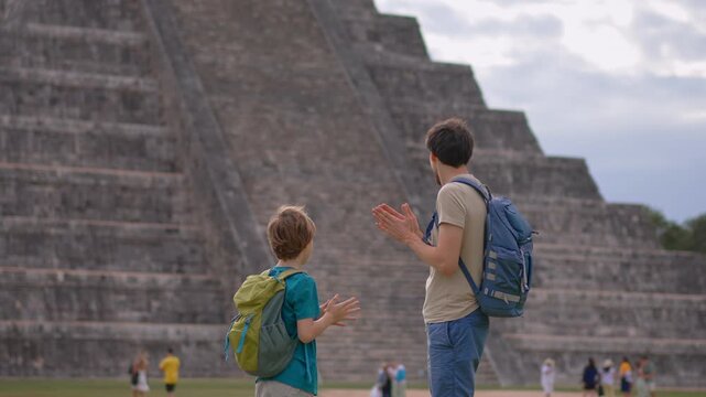 Father and son clapping hands in front of Kukulkan pyramid in Chichen Itza, Mexico. Happy family enjoying travel and cultural landmark. Bonding, joy, tourism and vacation concept. Slowmotion video.