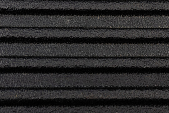 Close-up texture of a black ribbed rubber mat or tough plastic truck bed liner with a rough, non-slip surface.