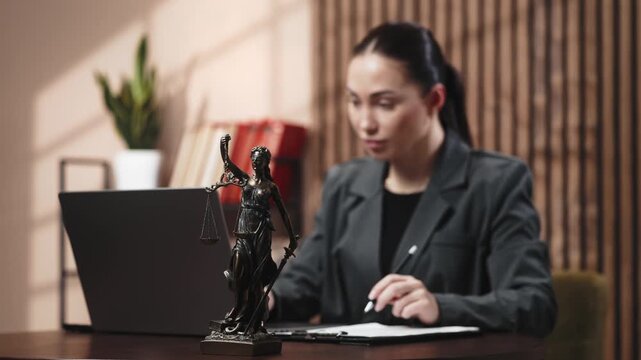Focused female lawyer working on laptop, analyzing legal documents and verifying data in modern office. Concept legal consulting, corporate law and professional accuracy.
