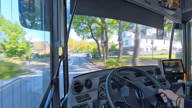 Perspektive aus dem Bus-Cockpit Busfahrer lenkt Linienbus bei Sonnenschein durch eine idyllische, gr&uuml;ne Wohnstra&szlig;e