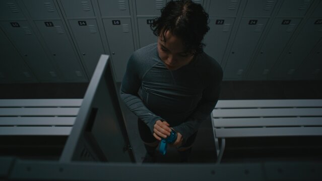 Woman in Sportswear Gets Ready in Gym Locker Room. Girl Puts on Athletic Top and Prepares to Drink Water From Blue Bottle. Fitness Motivation, Wellness, and Sports Related Storytelling. High Angle.