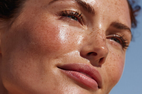 Close up freckled woman face with glowing skin, natural makeup, sunlit cheek and smooth texture conveying confidence and calm expression
