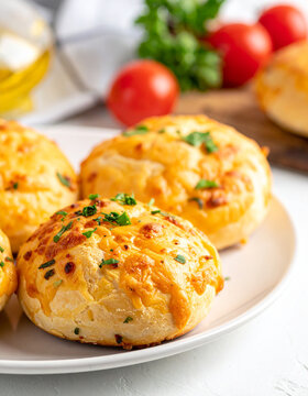 Cheesy bread buns with tomatoes and parsley on plate, tasty bakery, delicious food, fresh textures, appetizing dish, white putty table. Close-up.