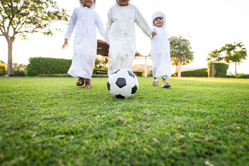 Obraz premium Arab kids wearing traditional emirati clothing meeting and having fun outdoors - Middle eastern boys bonding at the park in Dubai