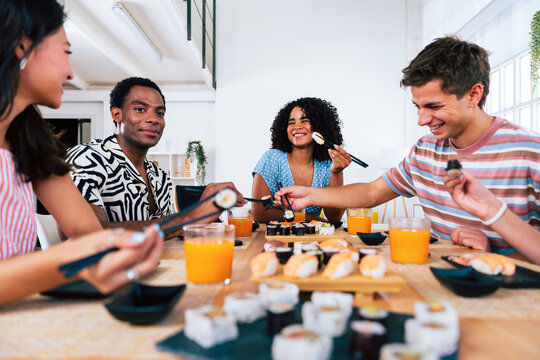 Multiethnic group of young friends meeting at home and eating sushi- Happy multiracial students having japanese cuisine dinner party