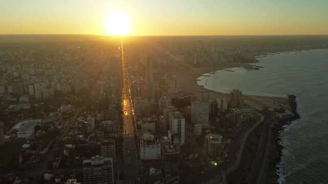 Drone aerial footage of golden hour sunset over Col&oacute;n Avenue and the coastline of Mar del Plata, Argentina, with Torre&oacute;n del Monje and Atlantic Ocean during winter. Urban coastal cityscape in South Am