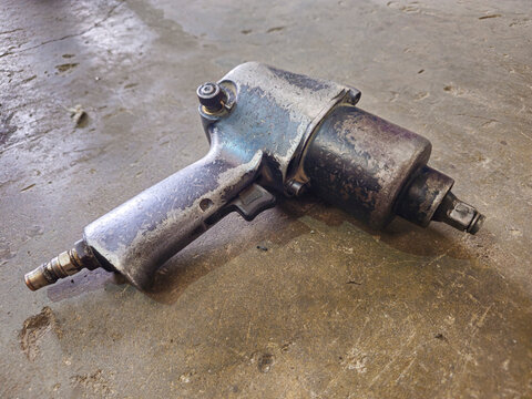 Old used pneumatic air impact wrench placed on a rough concrete floor