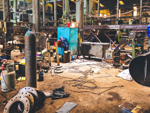 Interior view of a cluttered heavy industrial workshop with gas cylinders, flanges, and welding equipment