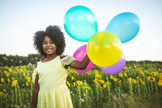 Pretty young african girl in a sunflowers field in bloom  playing with air balloons for her birthday party