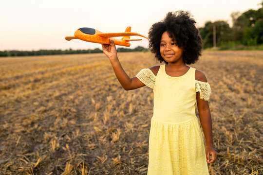 Pretty young african girl playing with airplane toy in the nature, concepts about sustainable lifestyle, green mobility and alternative transportation