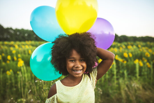 Pretty young african girl in a sunflowers field in bloom  playing with air balloons for her birthday party