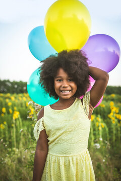 Pretty young african girl in a sunflowers field in bloom  playing with air balloons for her birthday party